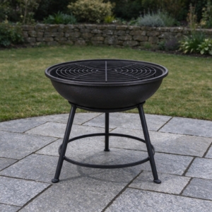 Cast iron fire bowl with grill grate in a black stand on granite setts