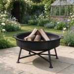 Black steel folding fire bowl with logs on a sandstone patio in a cottage garden