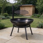 Steel fire pit with swing-arm cooking grill on stone paving in a family garden